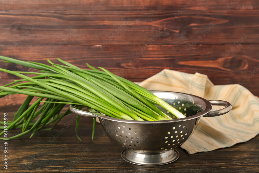 Colander with fresh green onion on wooden background