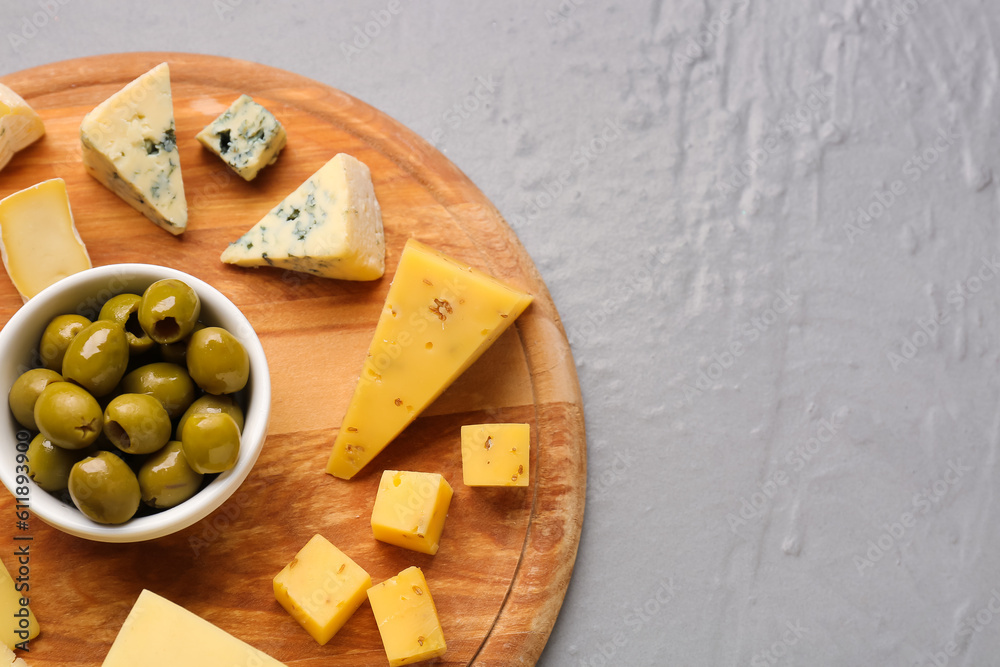 Wooden board with pieces of tasty cheese on grey background, closeup