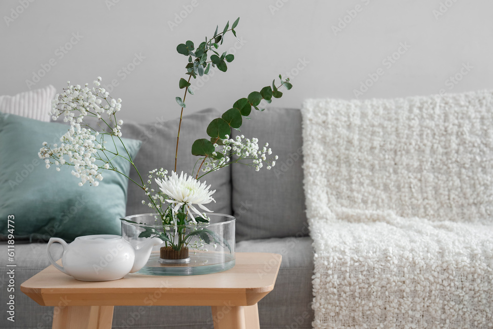 Beautiful ikebana with teapot on table in living room