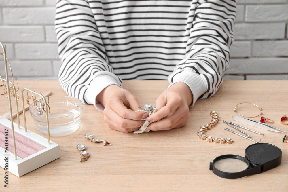 Woman cleaning beautiful jewelry at wooden table