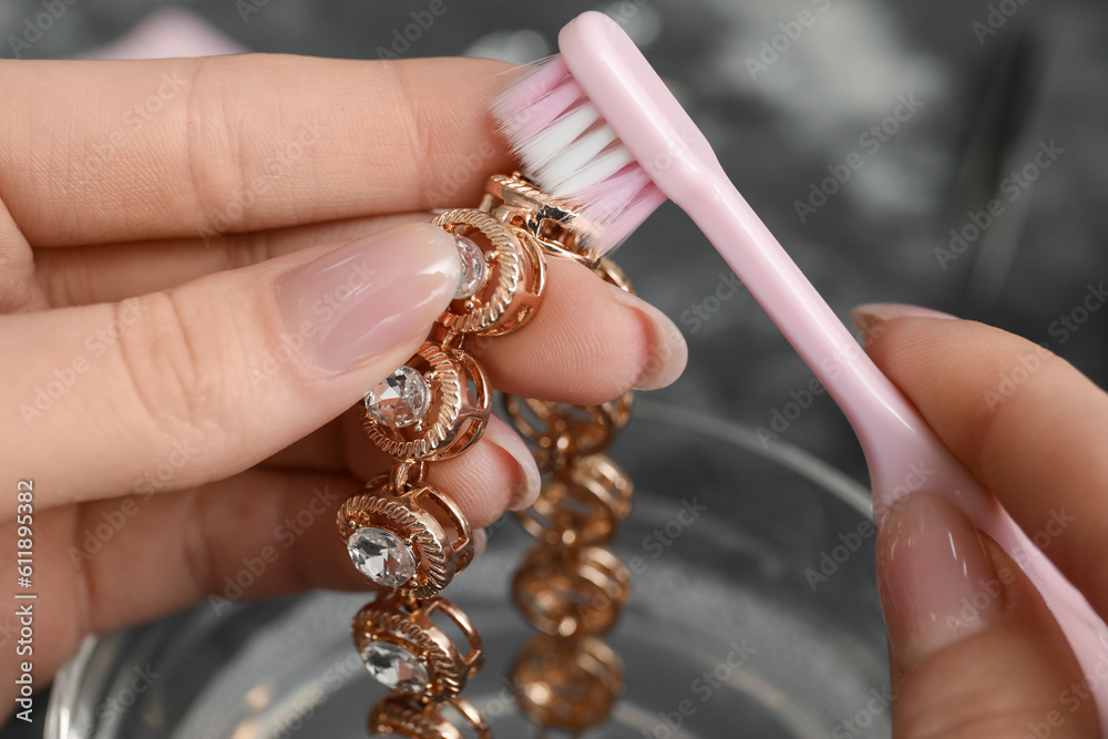 Woman cleaning beautiful bracelet with toothbrush, closeup