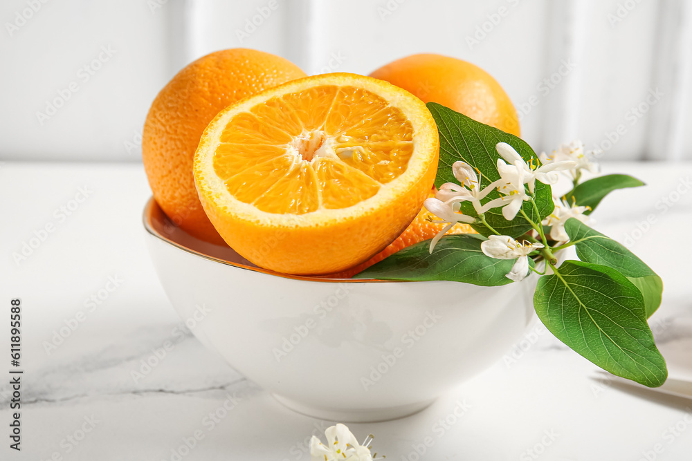 Bowl of oranges with blooming branches on white table