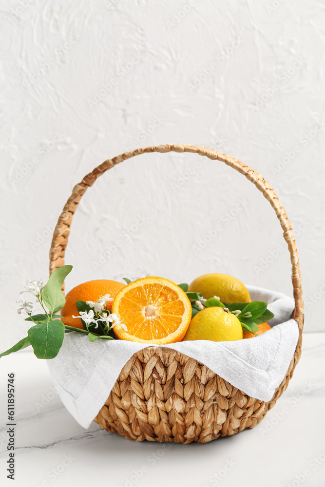 Basket of oranges and lemons with blooming branches on white table