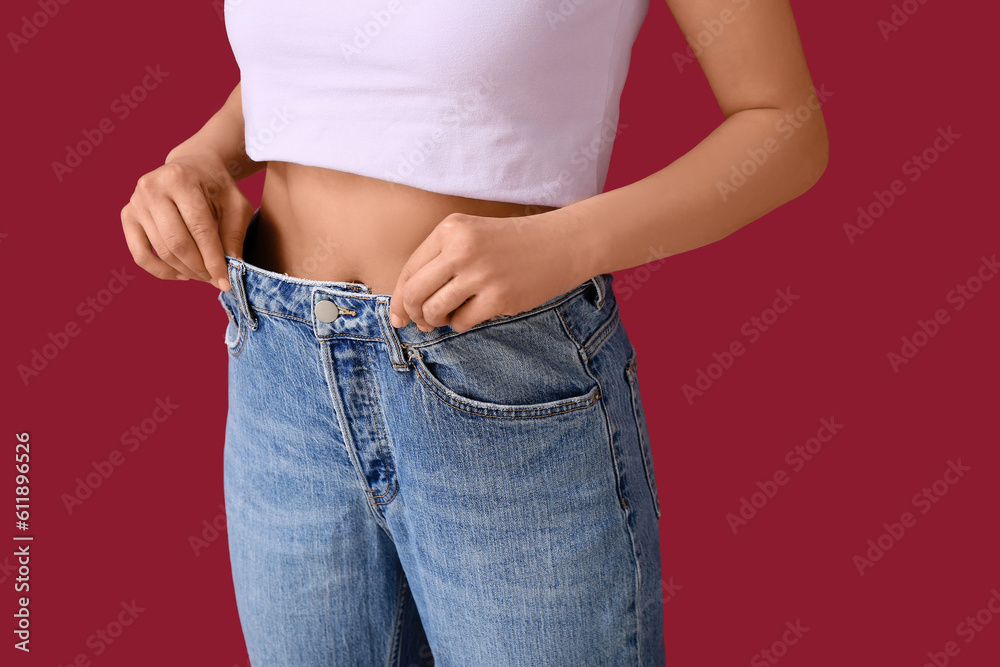 Young woman in loose jeans on burgundy background. Diet concept