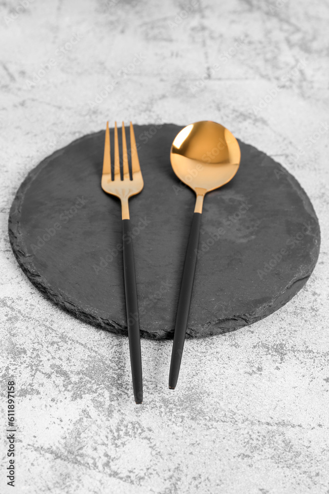 Board with golden spoon and fork on grey background