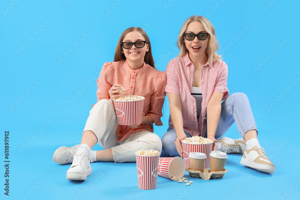 Young sisters in 3D glasses with popcorn on blue background