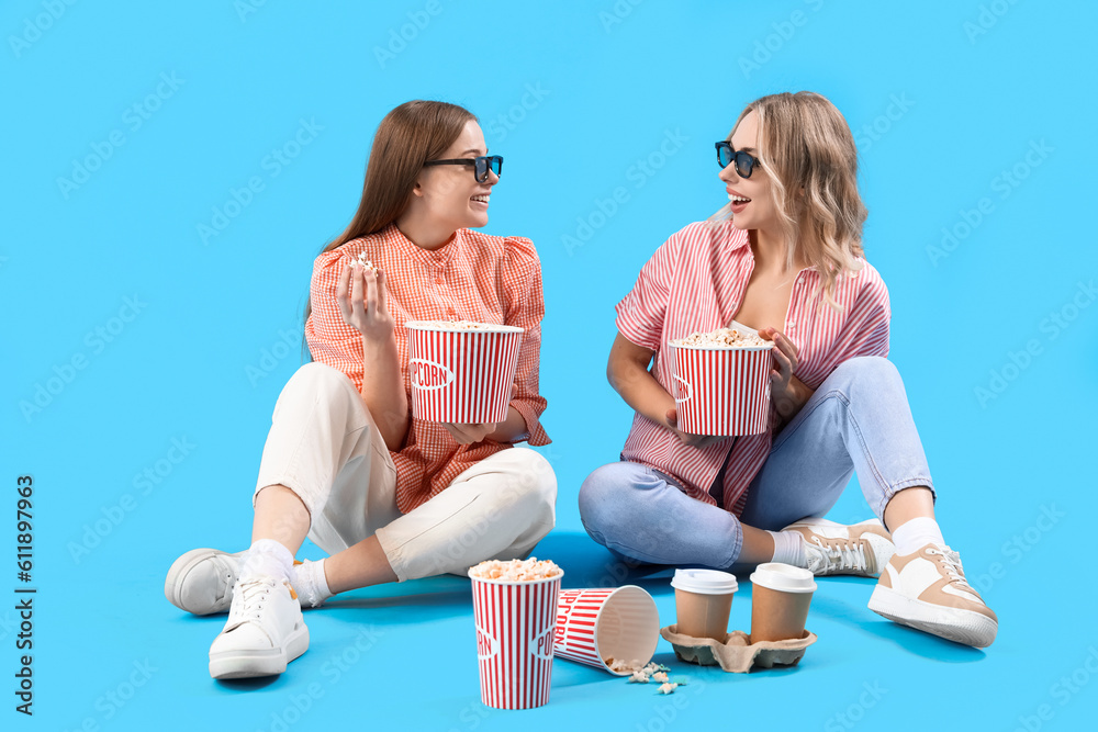 Young sisters in 3D glasses with popcorn on blue background