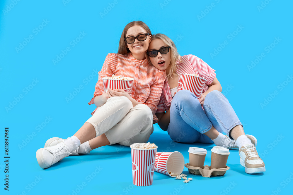 Young sisters in 3D glasses with popcorn on blue background