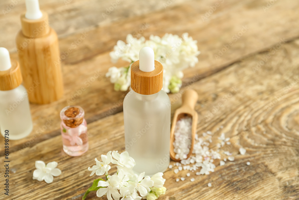 Bottles of cosmetic oil with beautiful lilac flowers and sea salt on wooden table