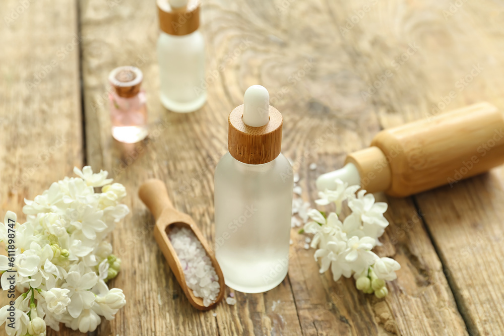 Bottles of cosmetic oil with beautiful lilac flowers and sea salt on wooden table