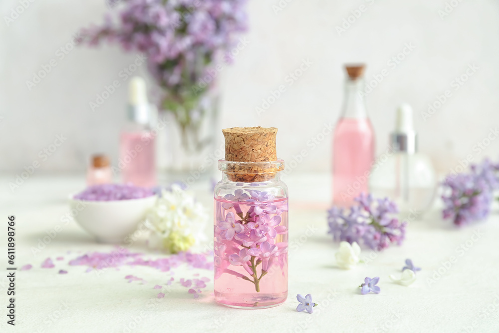 Bottles of cosmetic oil with beautiful lilac flowers and sea salt on white table