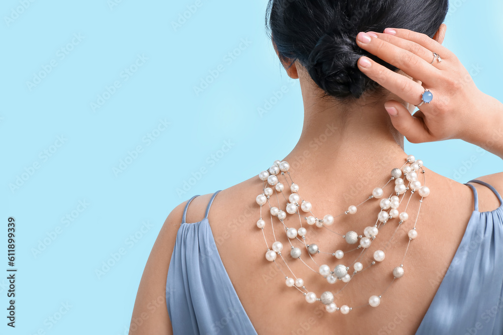 Young woman with beautiful jewelry near blue wall, back view