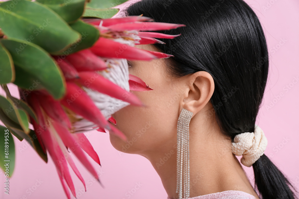 Profile of beautiful young woman wearing stylish earrings with protea flower near pink wall