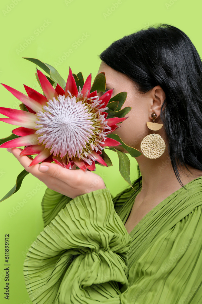 Profile of beautiful young woman wearing stylish earrings with protea flower near green wall