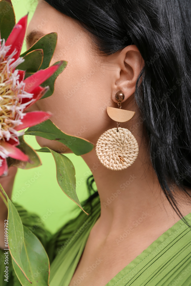 Profile of beautiful young woman wearing stylish earrings with protea flower near green wall