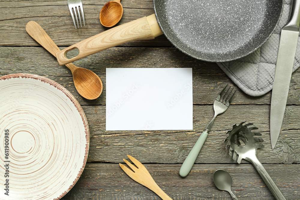 Blank card and different kitchen utensils on wooden background