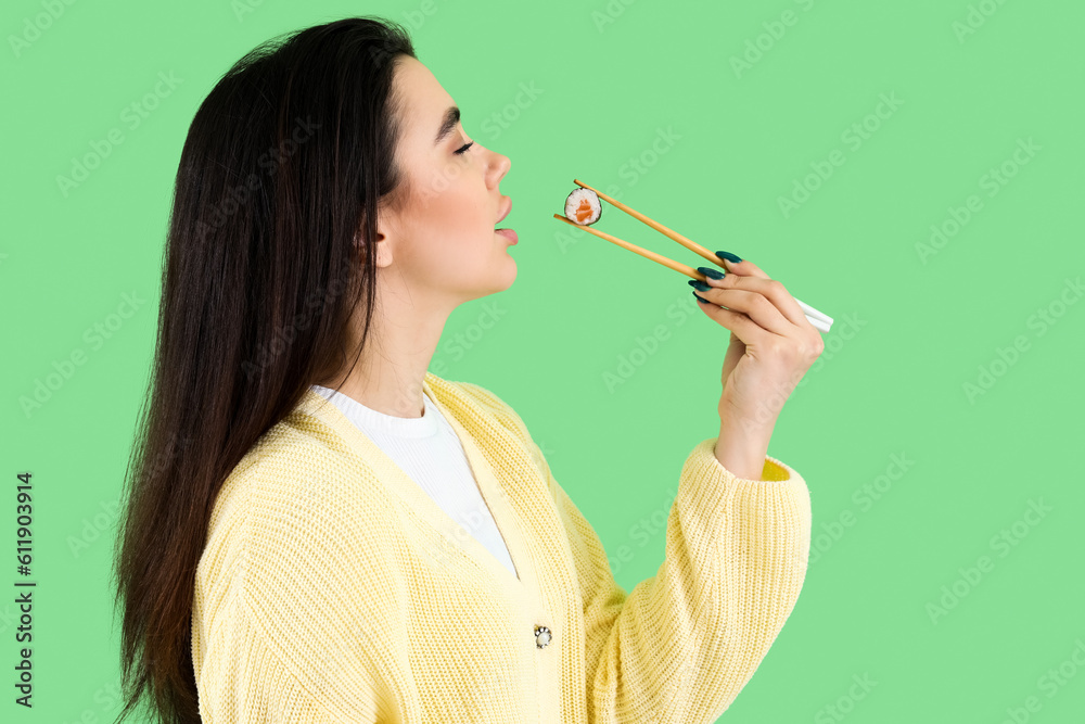 Young woman eating sushi roll on green background