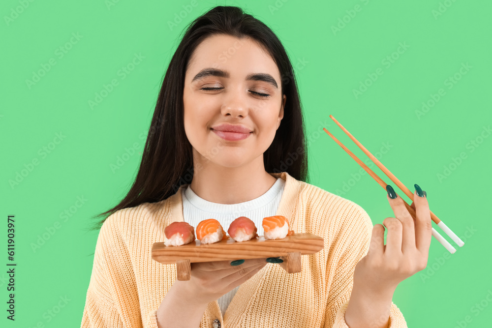 Happy young woman with sushi and chopsticks on green background