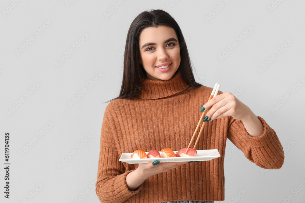 Young woman with sushi on light background