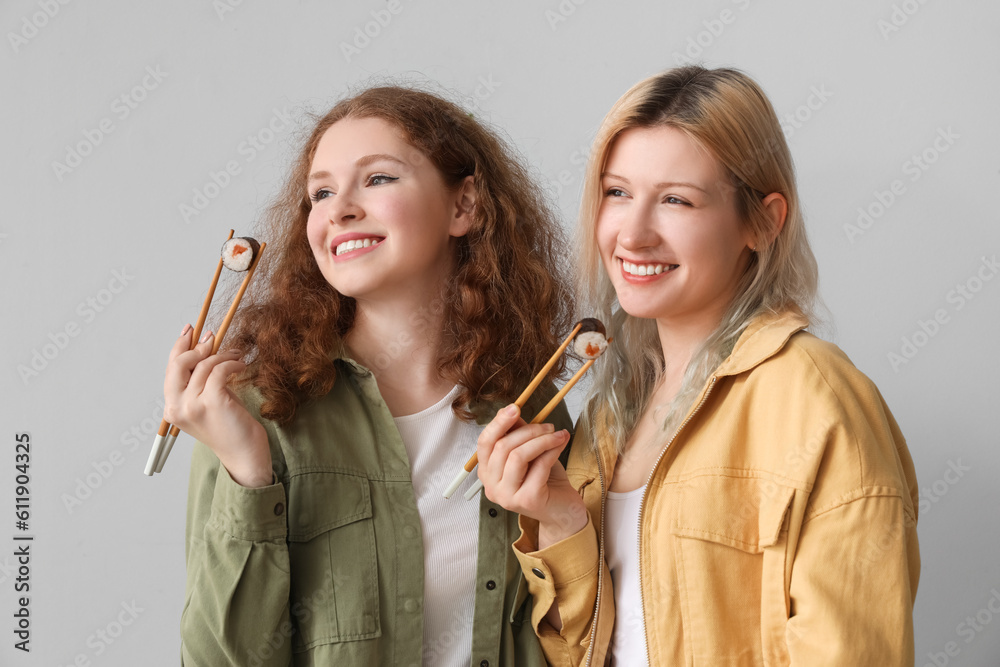 Young women with sushi rolls on light background