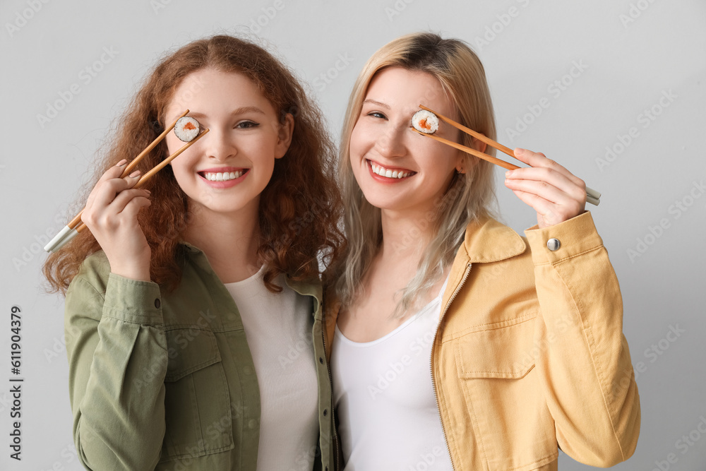 Young women with sushi rolls on light background