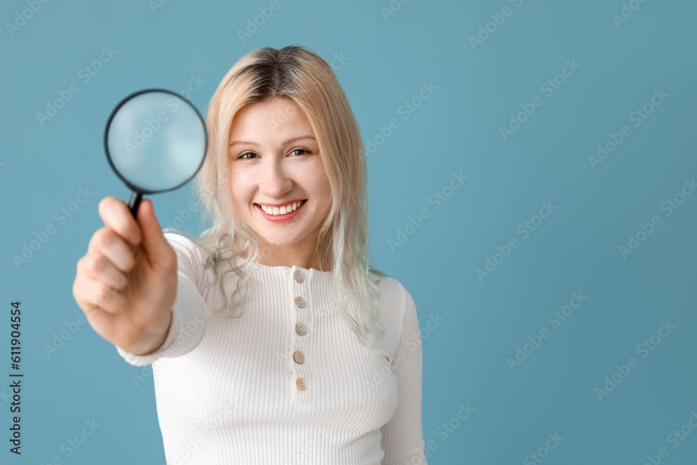 Young woman with magnifier on blue background, closeup