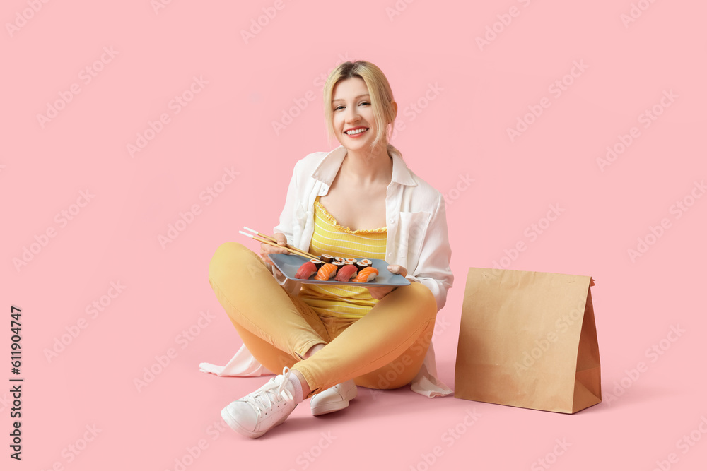 Young woman with sushi and paper bag sitting on pink background