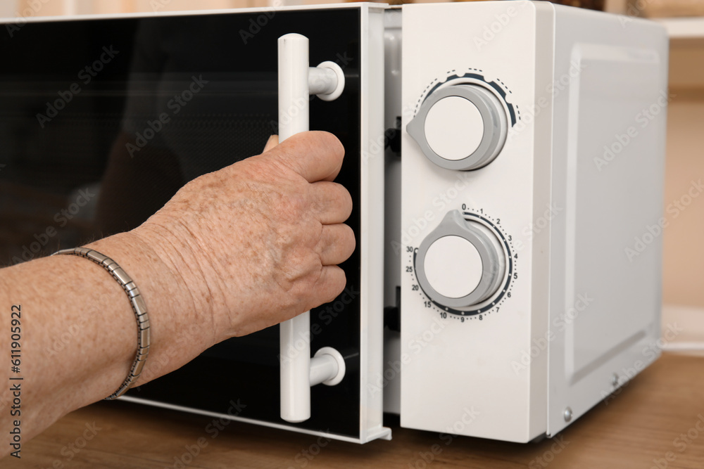 Senior woman opening microwave oven in kitchen, closeup