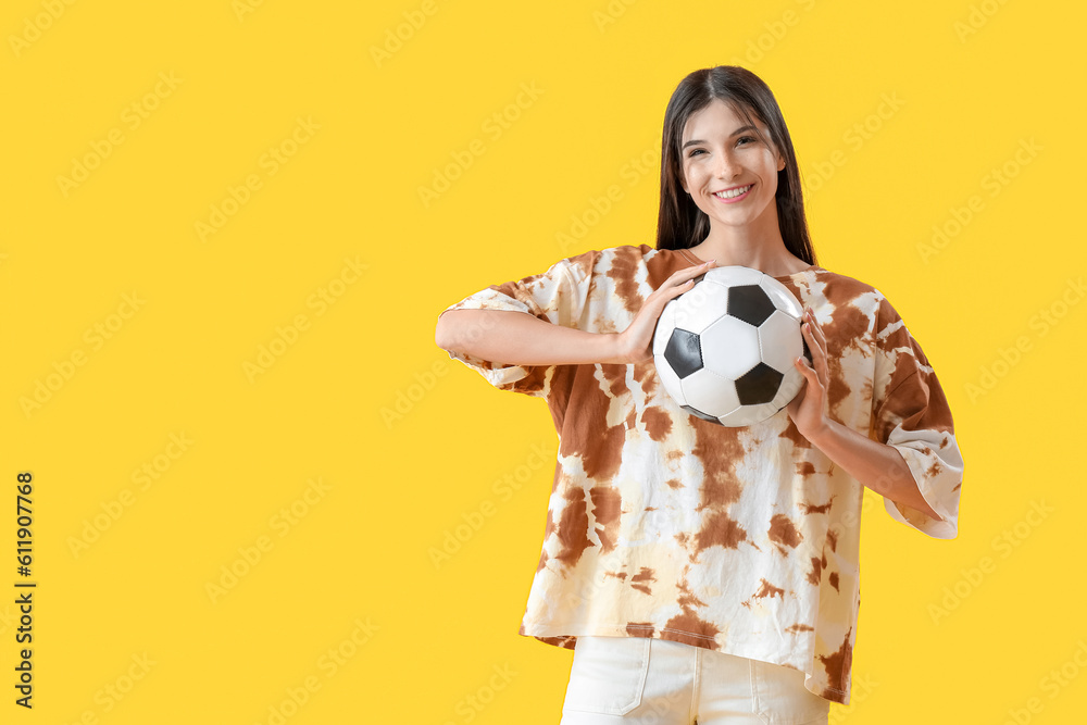 Young woman with soccer ball on yellow background