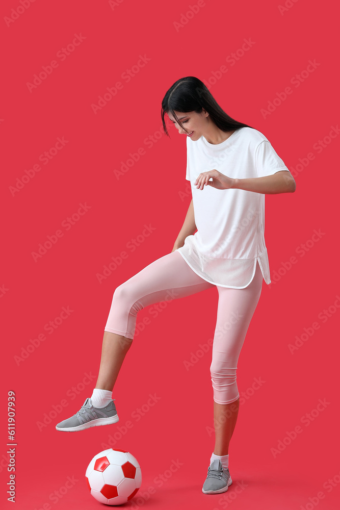 Young woman playing with soccer ball on red background