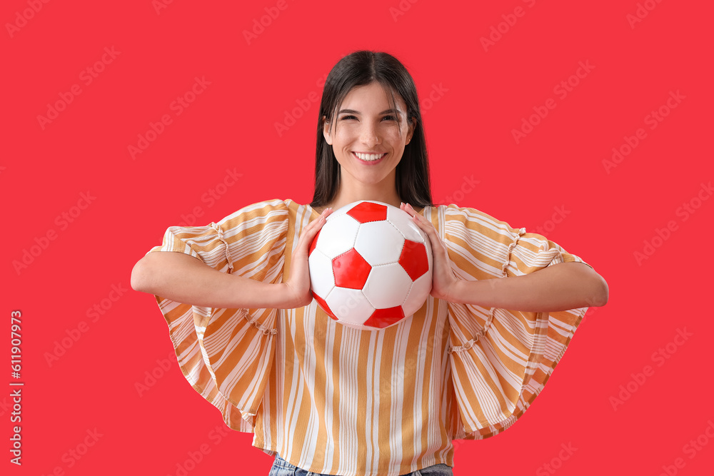 Happy young woman with soccer ball on red background