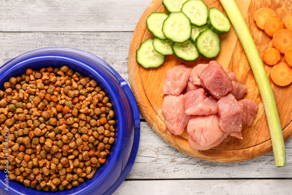 Bowl with dry pet food, raw meat and natural products on light wooden background