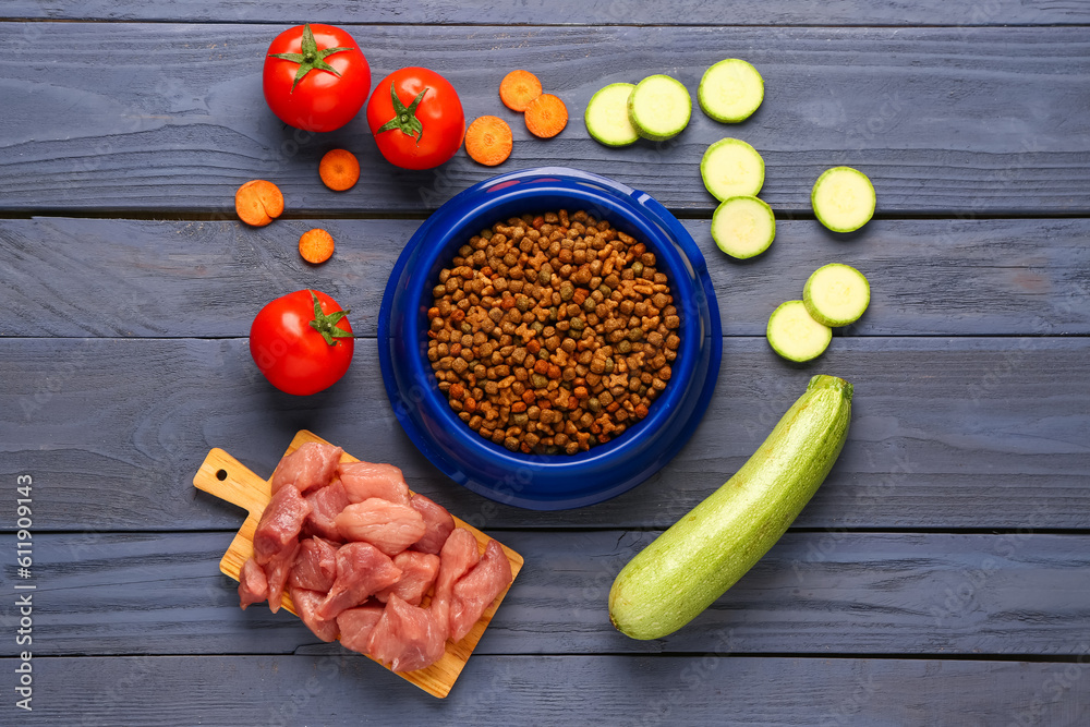 Composition with dry pet food, raw meat and natural products on color wooden background