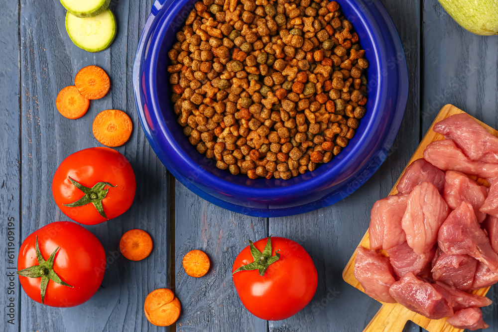 Bowl with dry pet food, raw meat and natural products on color wooden background, closeup