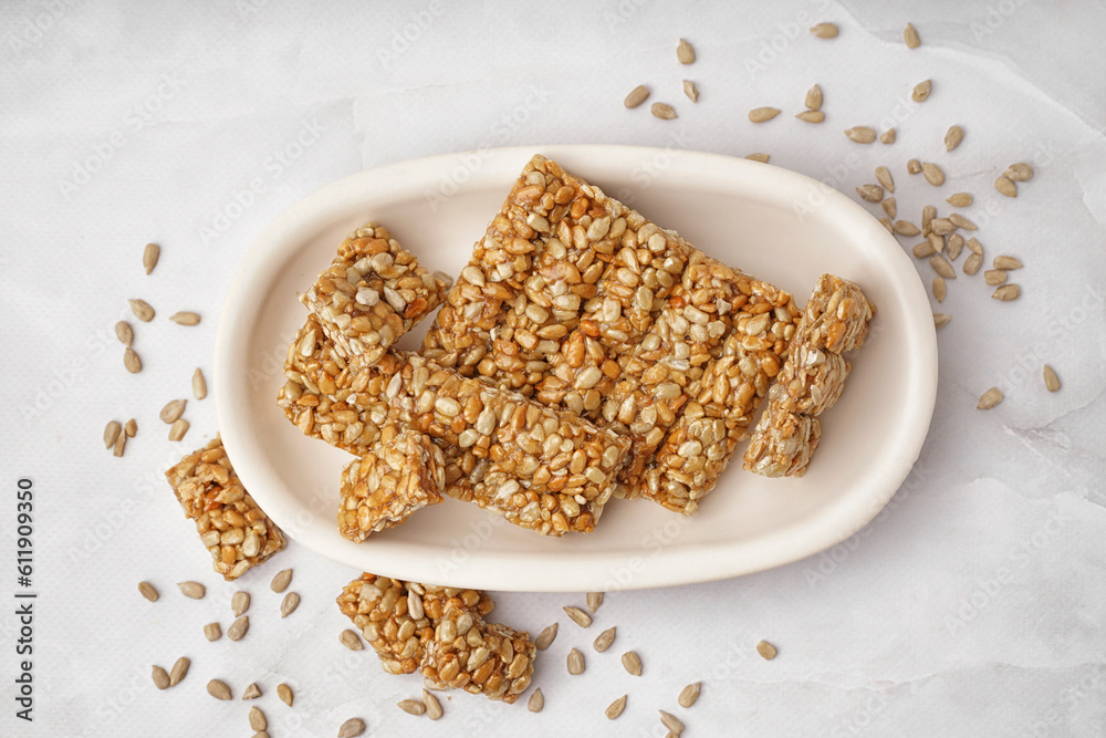 Plate with tasty pieces of kozinaki and sunflower seeds on white background