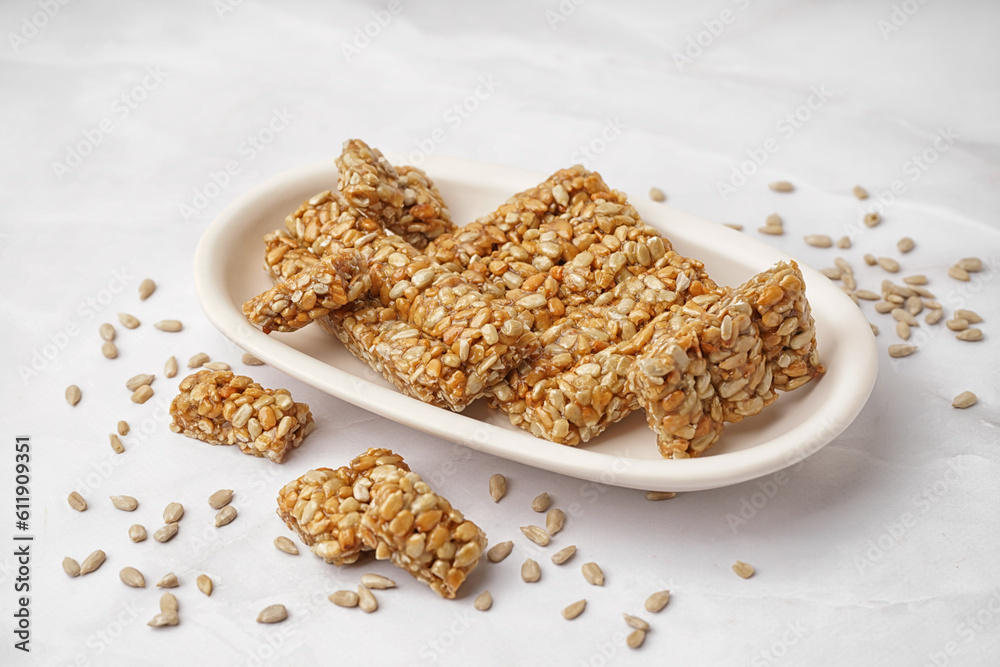 Plate with tasty pieces of kozinaki and sunflower seeds on white background