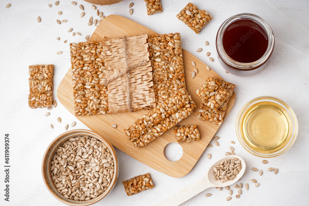 Wooden board with tasty kozinaki, honey and sunflower seeds on white background