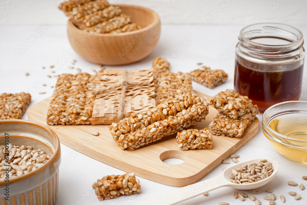 Wooden board with tasty kozinaki, honey and sunflower seeds on white background