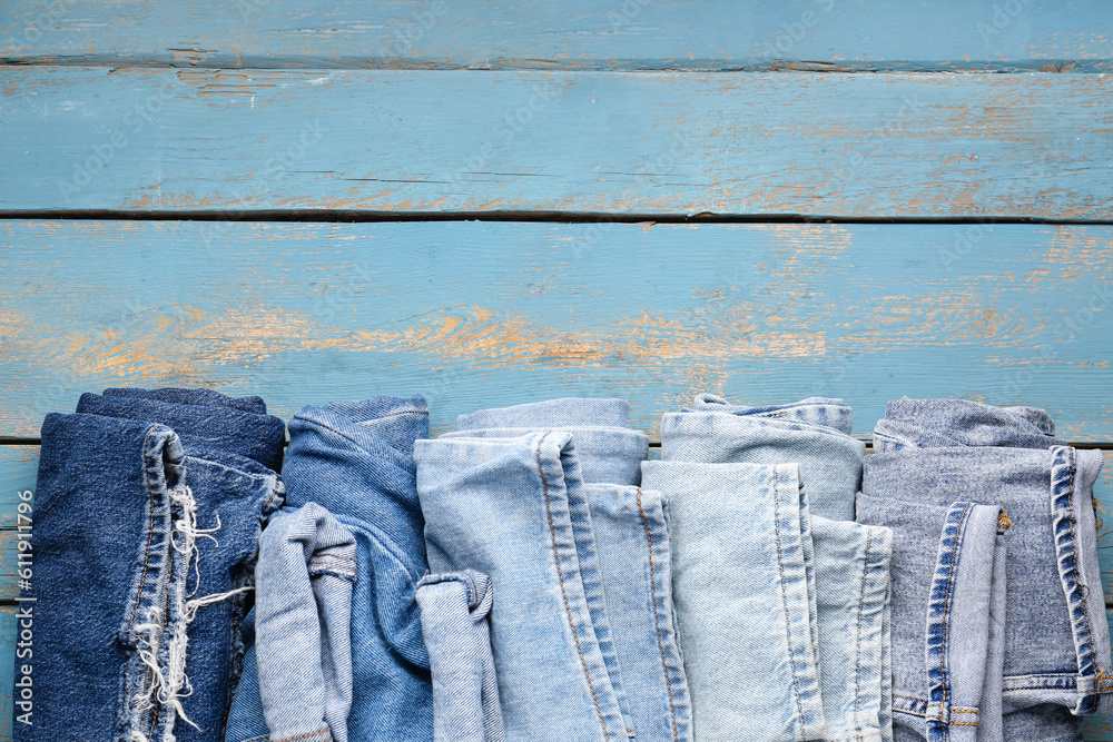 Different rolled jeans on blue wooden background, closeup