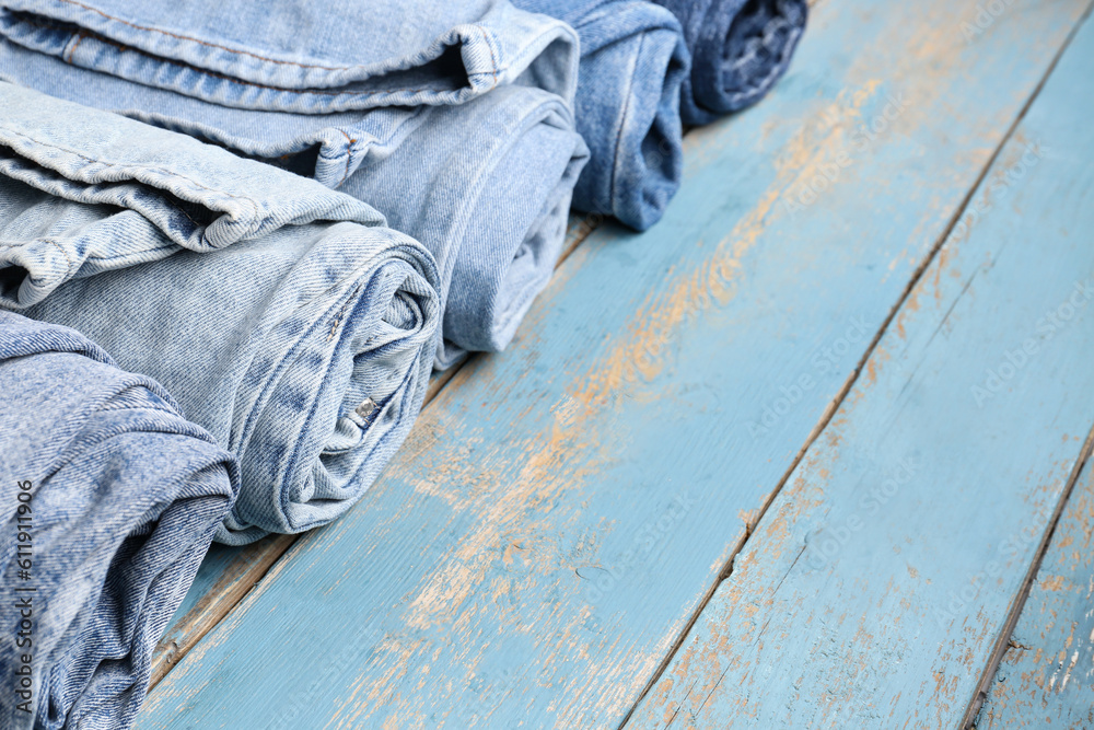 Different rolled jeans on blue wooden background, closeup