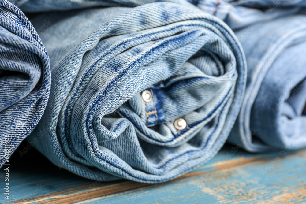 Different rolled jeans on blue wooden background, closeup