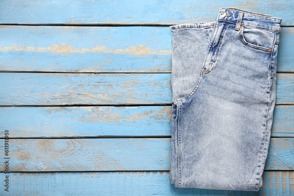 Stylish denim jeans on blue wooden background