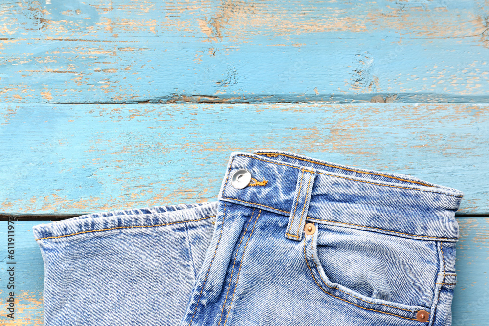 Stylish denim jeans on blue wooden background