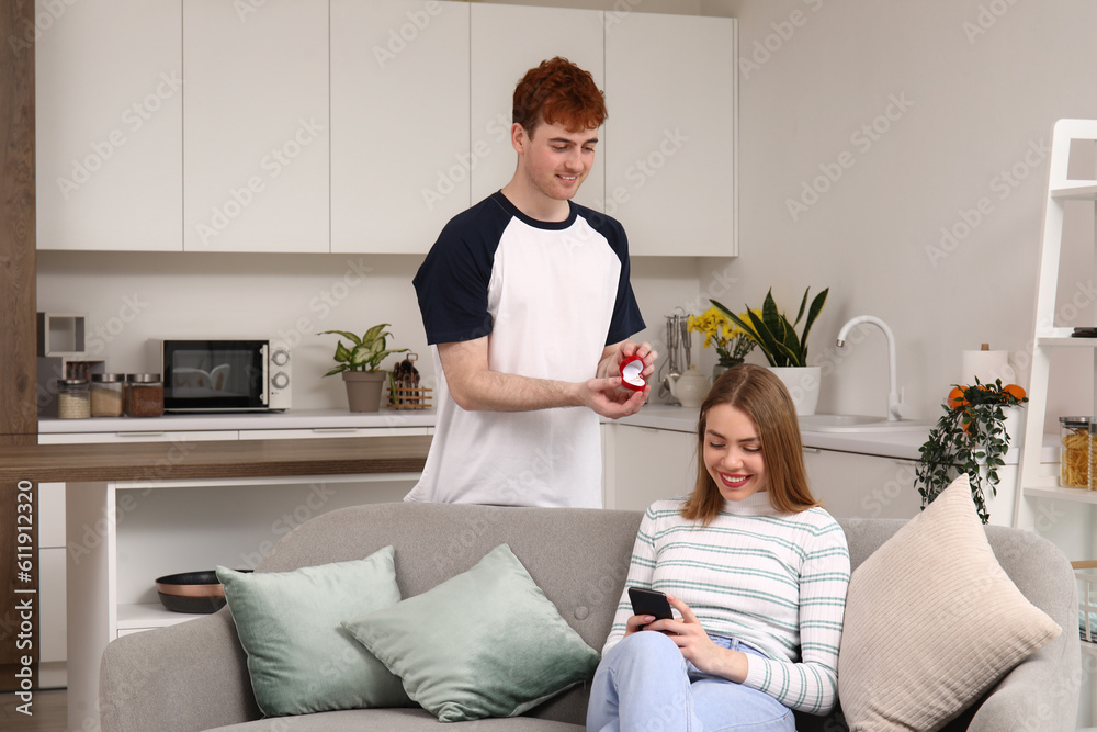 Young man proposing to his girlfriend using mobile phone in kitchen