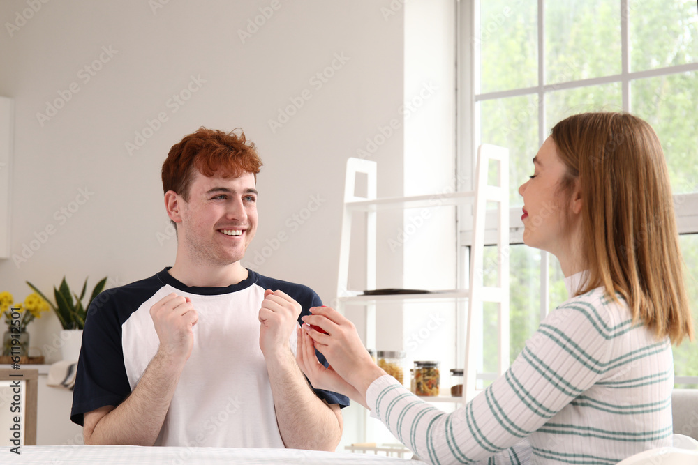 Young woman proposing to her happy boyfriend in kitchen