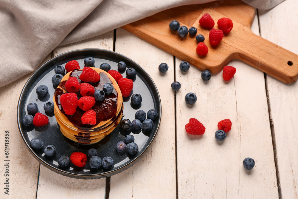 Plate with sweet pancakes and berries on light wooden background