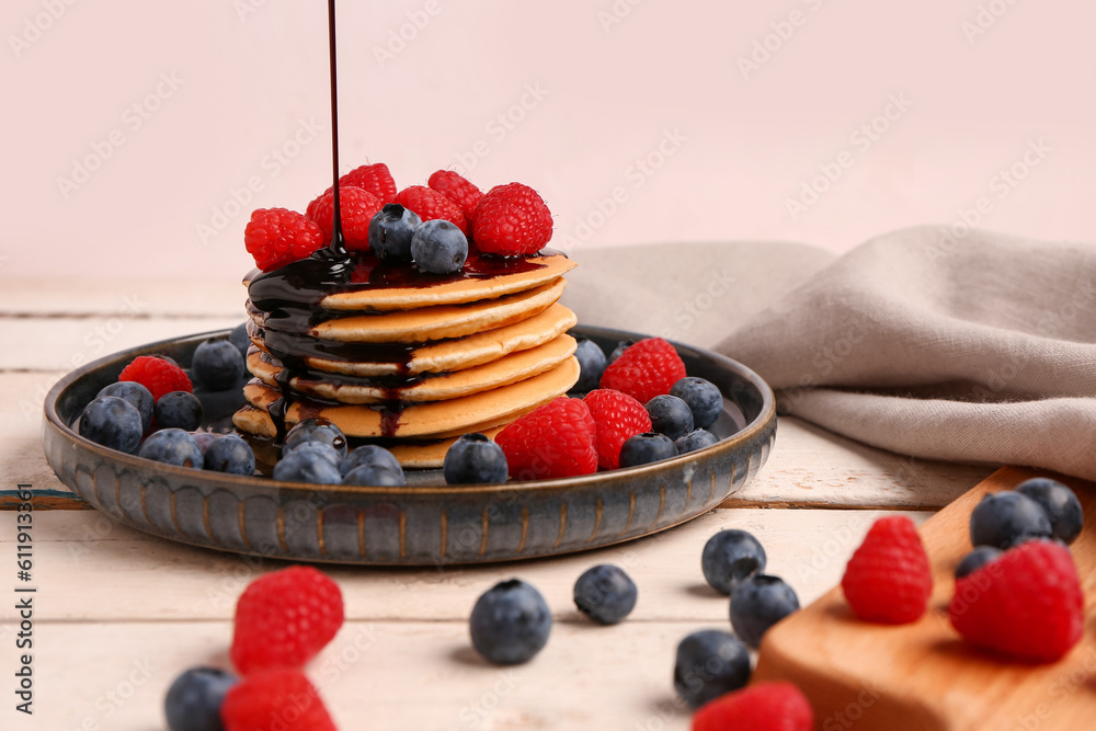 Plate with sweet pancakes and berries on light wooden background, closeup