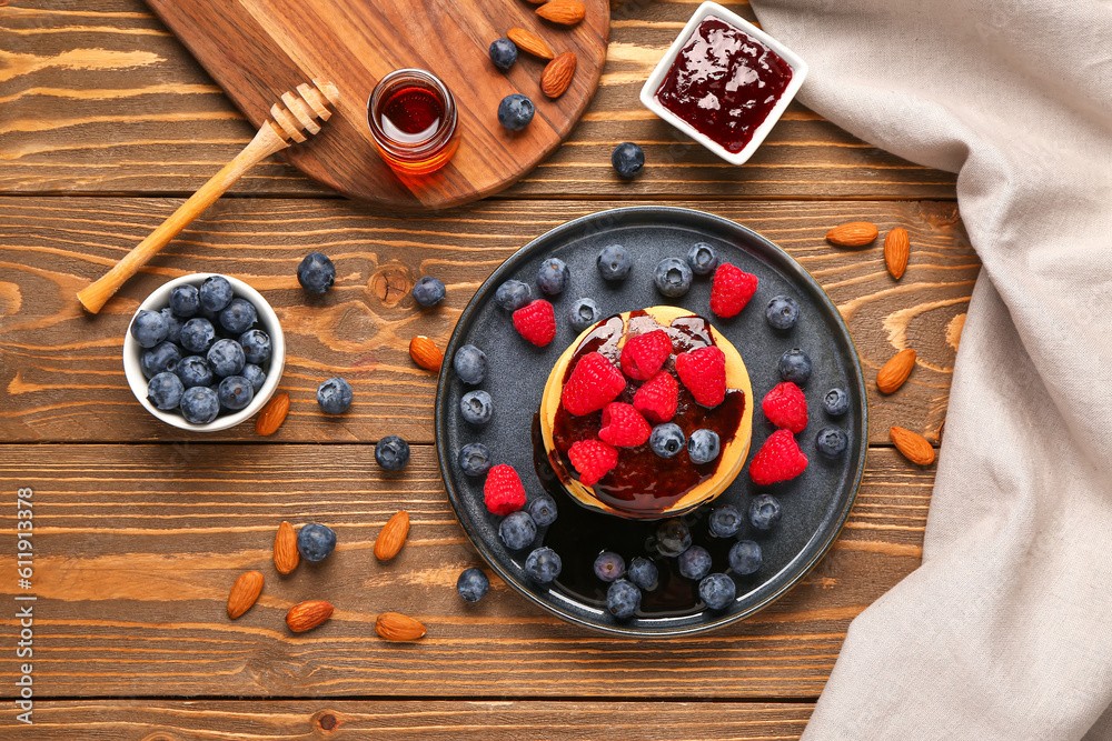 Plate with sweet pancakes, berries, nuts and jam on wooden background