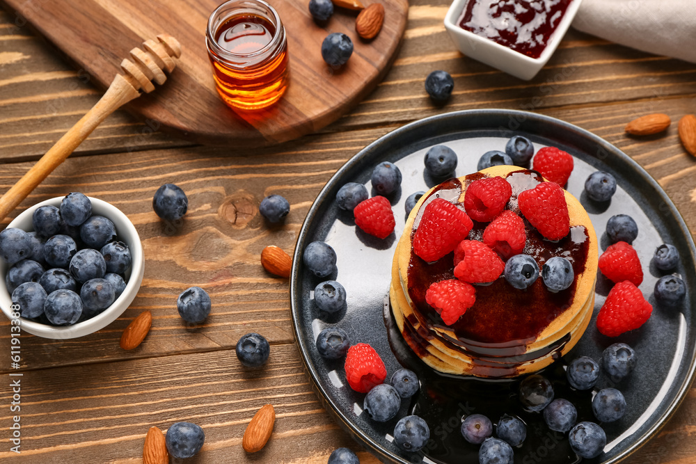 Plate with sweet pancakes, berries, nuts and jam on wooden background