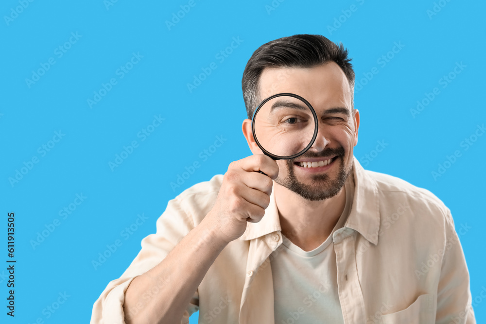 Handsome man with magnifier on blue background